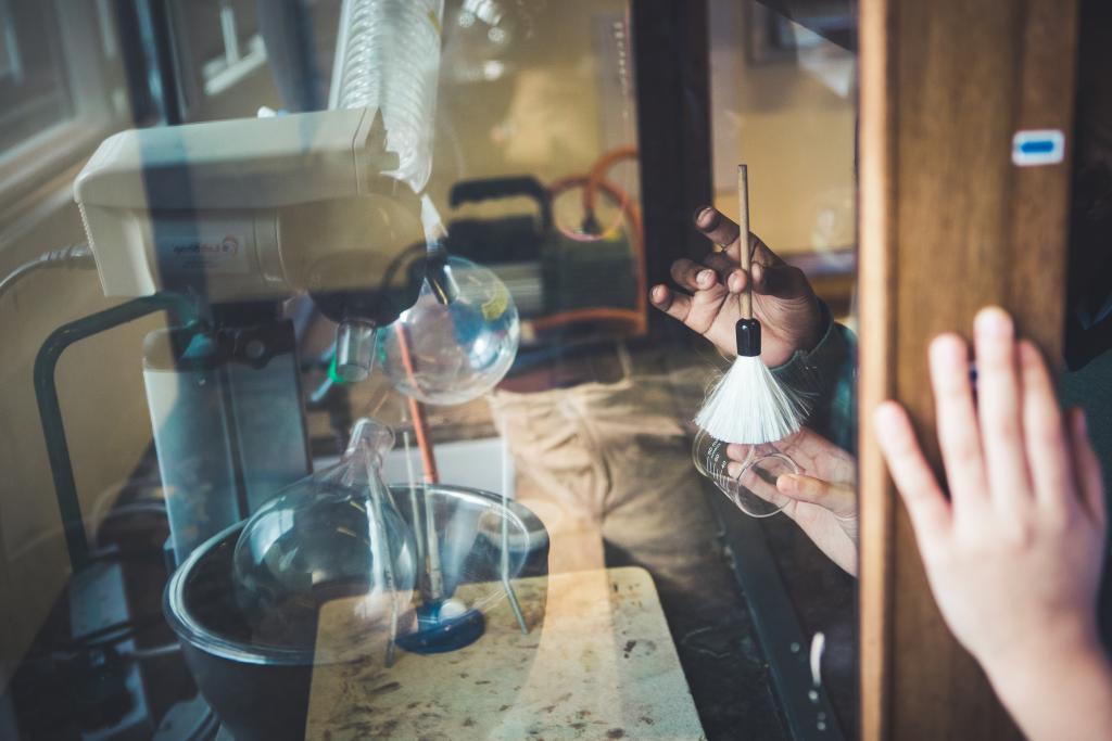 The hands of a CLC pupil dust for print, using a forensic fingerprint brush and a glass beaker, during a forensics chemistry lesson