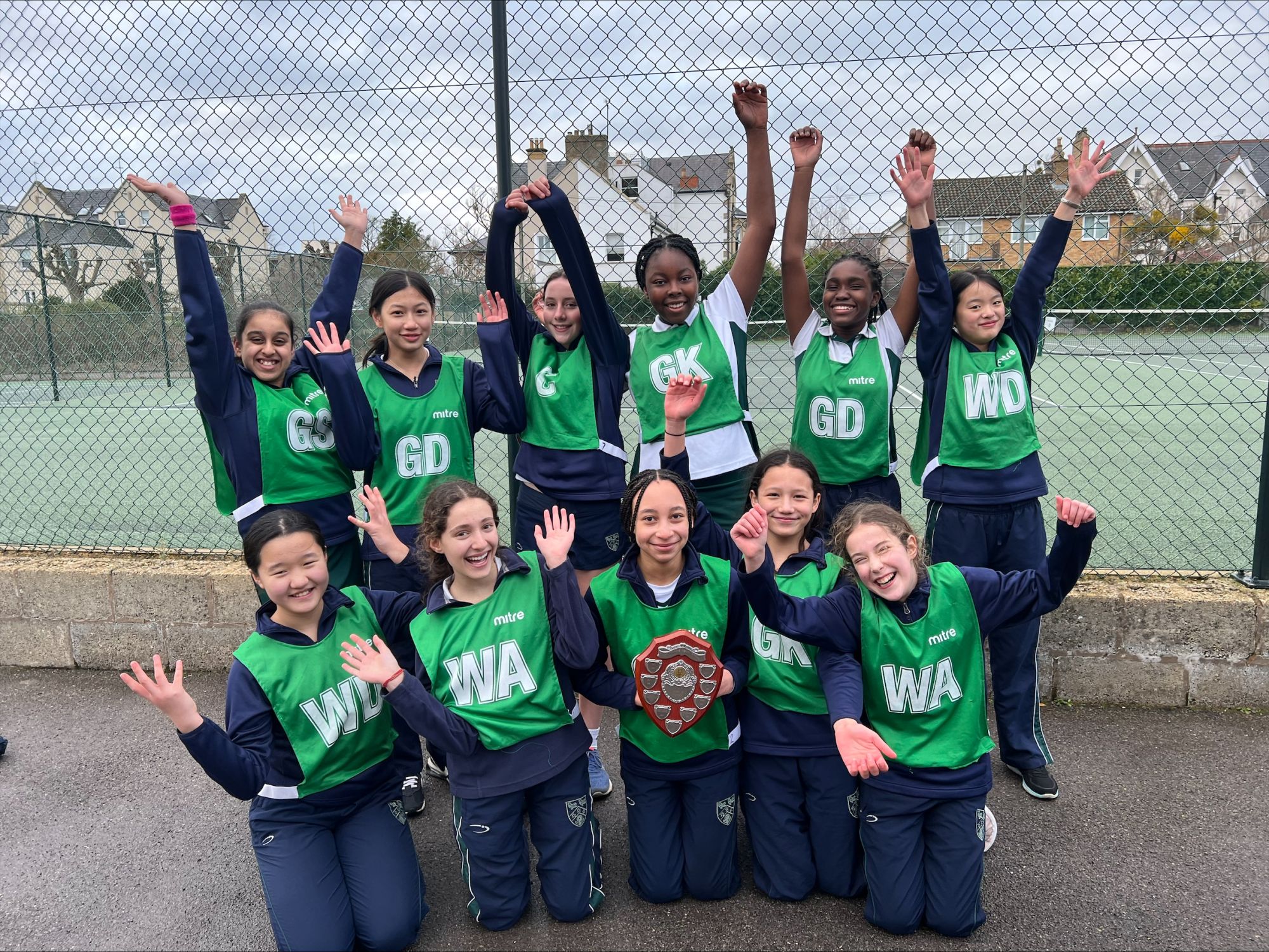 The U12 netball players celebrate with their hands in the air, with a player in the middle holding the award.